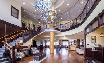 a grand staircase leads to a large , open lobby with a chandelier and wooden floors at The Inn at Harbor Shores