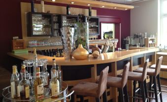 a modern bar with wooden counter , wine glasses , bottles , and various liquor bottles on shelves , accompanied by comfortable seating at Hotel Germania