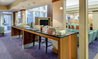 a hotel lobby with a long wooden table in the middle , surrounded by chairs and couches at Residence Inn Auburn