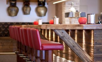 a modern bar with wooden walls , red stools , and gold accents , including a couple of lights hanging from the ceiling at Hotel Steinbock