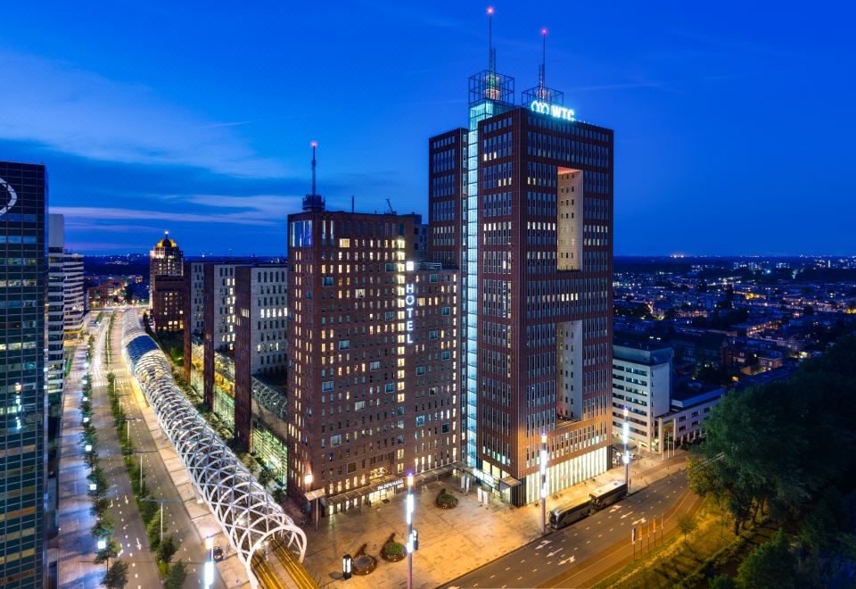 a city skyline at night , with several tall buildings lit up and a blue sky at NH Den Haag