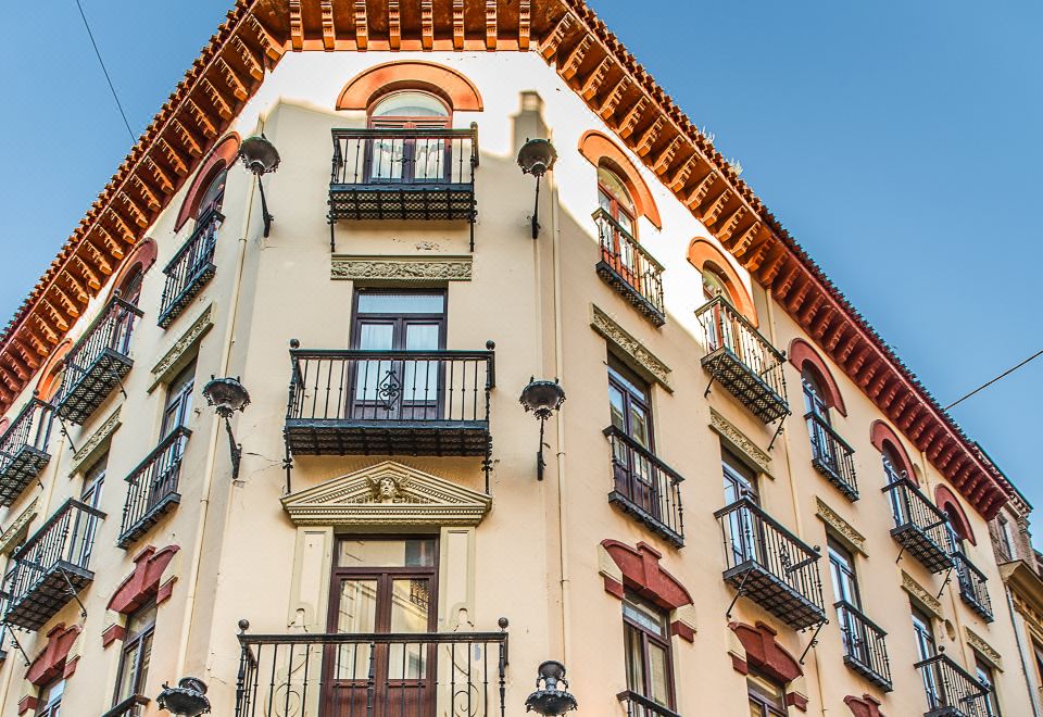 a large , white building with red trim and balconies , set against a clear blue sky at Hotel Inglaterra