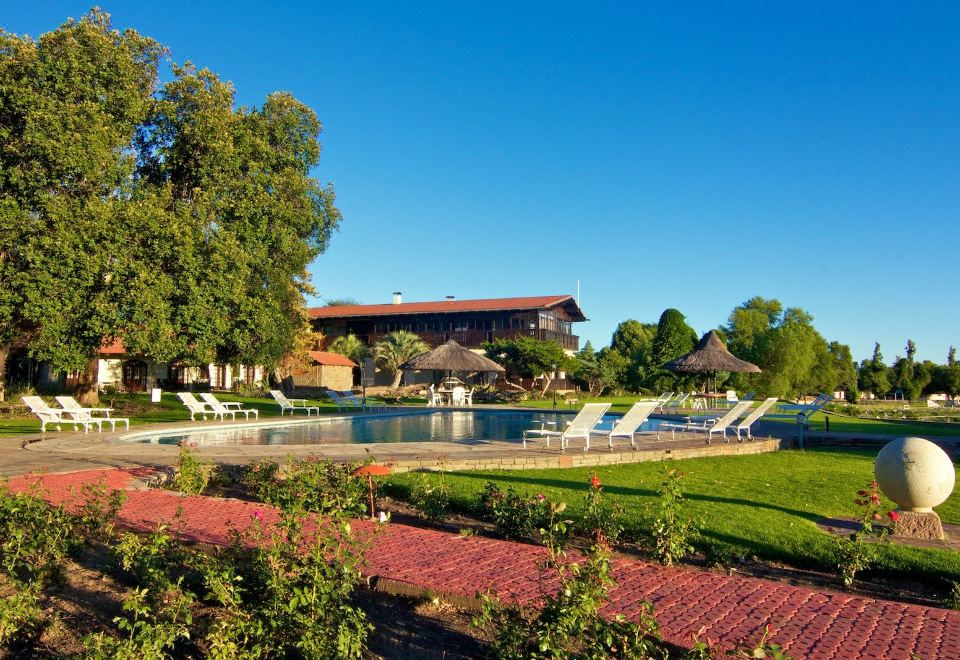 a resort with a large pool surrounded by grass , trees , and benches , under a clear blue sky at Midgard