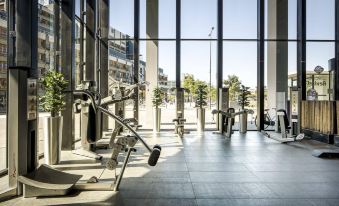 a well - equipped gym with various exercise equipment , including treadmills and weight machines , set up in front of large windows at Fletcher Wellness-Hotel Leiden