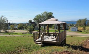 a wooden deck with a patio umbrella , surrounded by a grassy field and trees , under a clear blue sky at The Fiddle and the Sea Bed and Breakfast