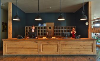 a man and a woman are standing behind a wooden reception desk in a hotel lobby at Rooms Hotel Kazbegi