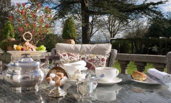 a table with a white cup and saucer , teapot , silverware , fruit , and other items is set up outside at Blaisdon House B&B