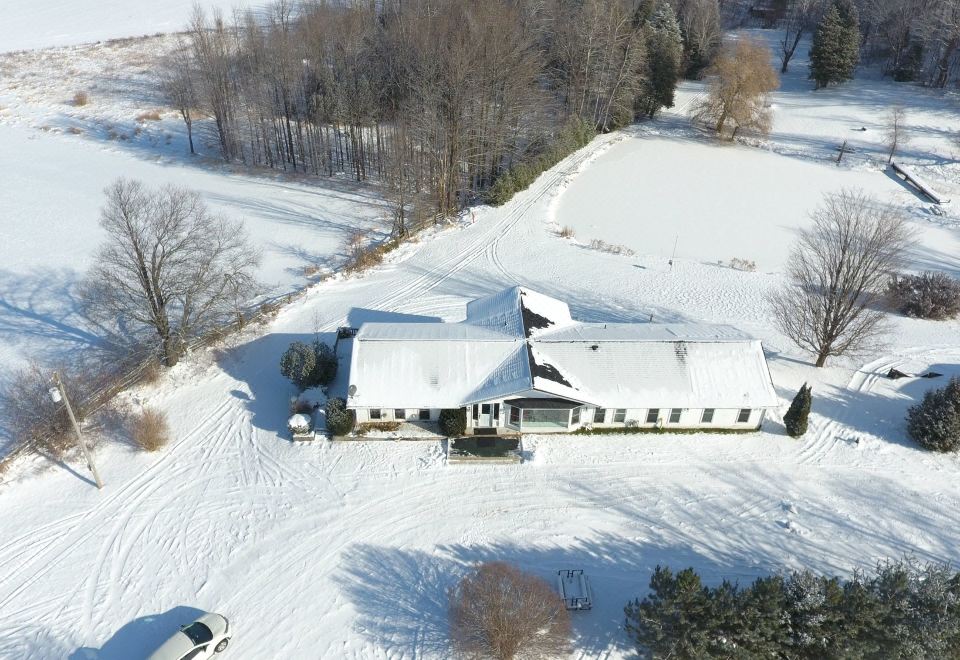 a snow - covered field with a large white building in the middle , surrounded by trees and other buildings at White House Farm