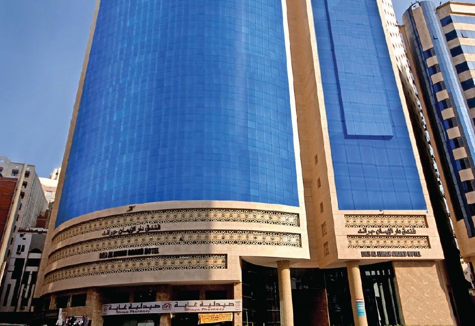 The large building with blue glass panels is located in front of other buildings at Emaar Grand Hotel