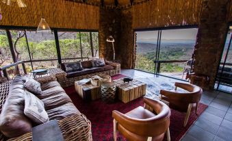 a spacious living room with a couch , chairs , and a view of the mountains outside the window at Leopard Mountain Safari Lodge