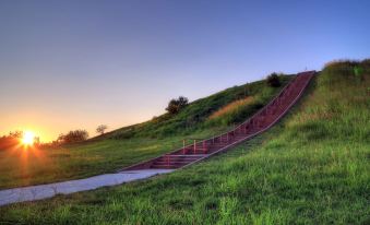 a grassy hill with a red staircase leading up to it , surrounded by green grass and trees at Green Tree Inn