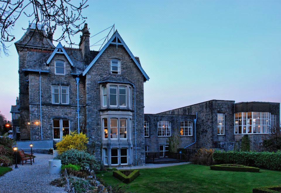 a large stone building with multiple windows and a garden , set against a blue sky at Cumbria Grand Hotel