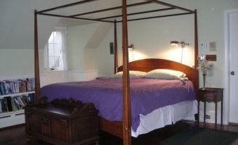 a wooden canopy bed in a bedroom , with a purple comforter and white sheets on it at Cobb Hill Estate