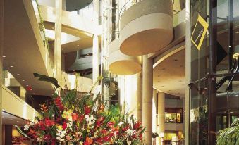a large , modern hotel lobby with high ceilings and greenery , as well as various potted plants and flowers at The Westin Bonaventure Hotel & Suites, Los Angeles