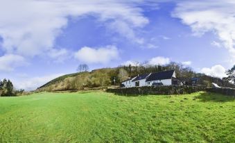 a house is situated on a hillside with green grass and trees in the background at YHA Brecon Beacons Danywenallt