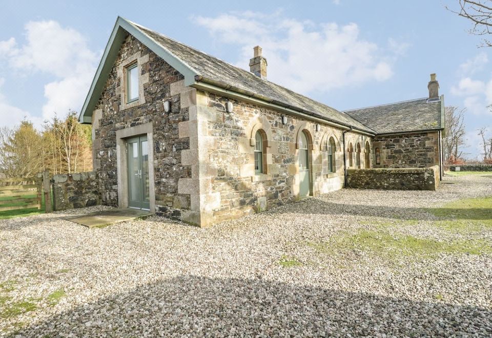 a stone building with a green door and arched windows , surrounded by gravel and trees at Kennels