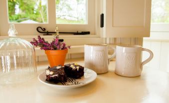 a white dining table with two white mugs and a plate of brownies on it at The Snug