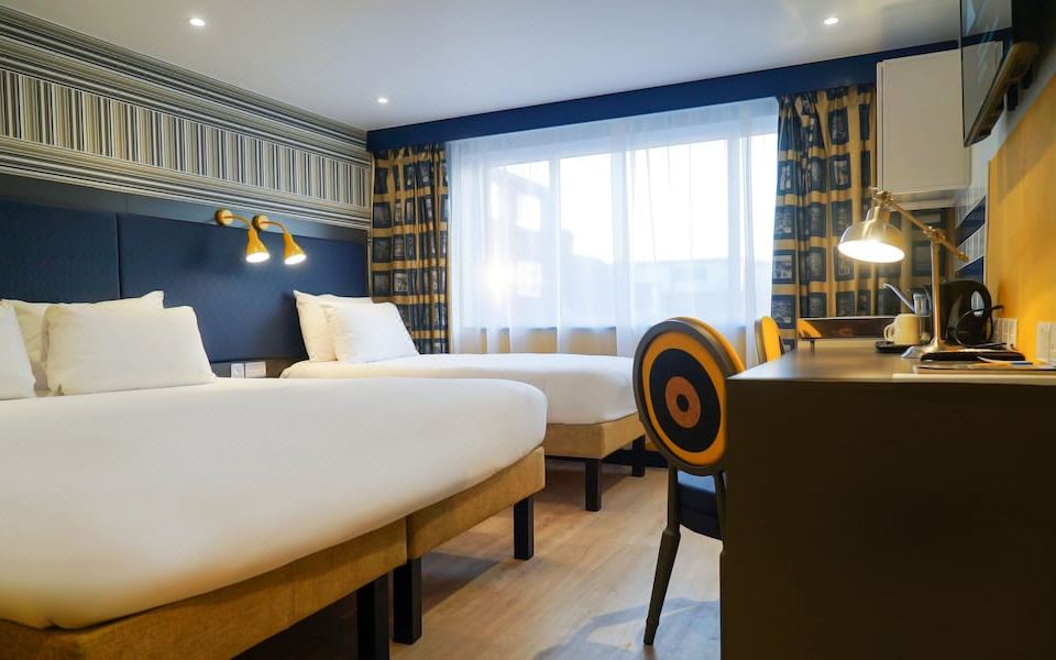 a modern hotel room with two beds , white bedding , and wooden flooring , along with a view of the city through large windows at Best Western Plus London Croydon Aparthotel