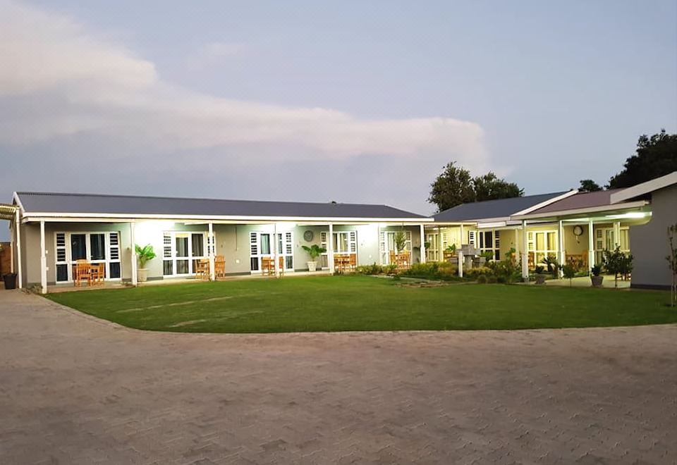 a large white building surrounded by grass and trees , with a well - maintained yard in front of it at Graceland Guesthouse