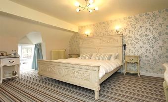 a large white bed with a striped carpet in the middle of a room , surrounded by white walls and a wooden floor at The Hand at Llanarmon