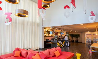a modern living room with red couches , pendant lights , and white walls , as well as a car parked in the background at Ibis Styles Piracicaba