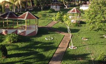 a lush green lawn with a wooden walkway leading to a gazebo , surrounded by trees and buildings at Paradise Reggae Resort
