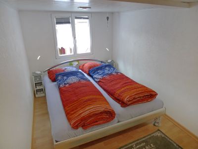 a bed with orange and blue bedding is situated in a small room next to a window at Marilyn Visperterminen