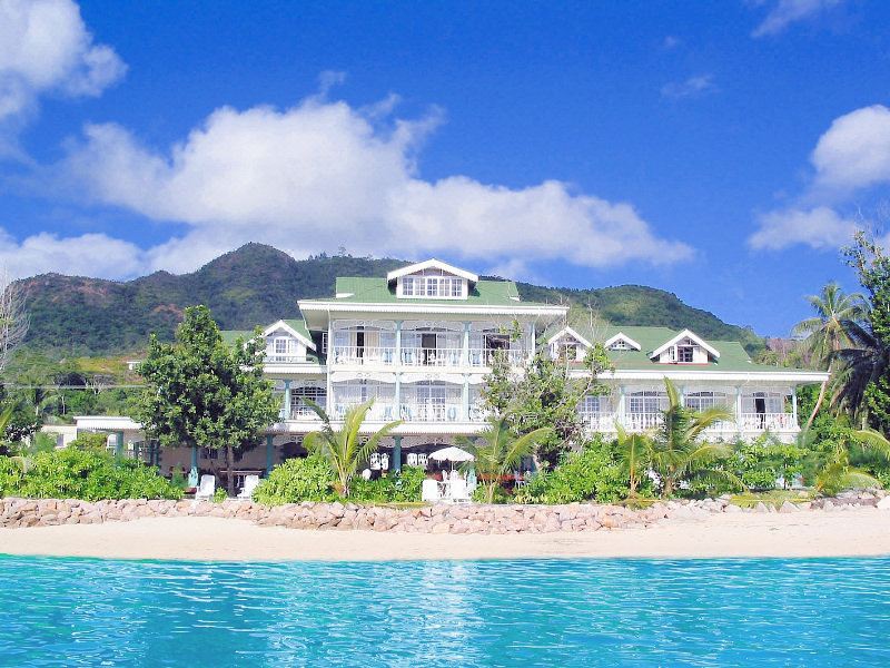 a large white house with a green roof is situated on a beach , surrounded by water at Palm Beach Hotel