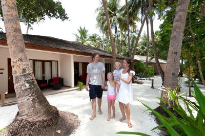 a family of four , consisting of a man , a woman , and two children , is walking together in front of a tropical beach house at Vilamendhoo Island Resort & Spa