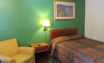 a hotel room with a green wall , wooden bed frame , and yellow armchair , along with a painting on the wall at Village Inn