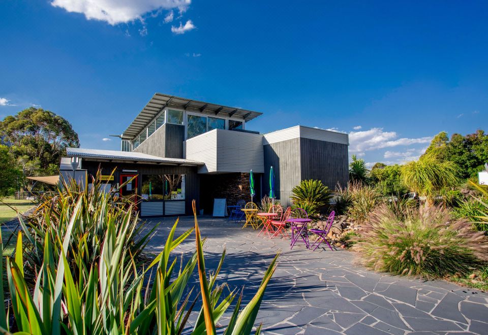 a modern house with a large window and patio furniture is surrounded by plants and flowers at Nrma Halls Gap Holiday Park