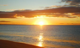 a beautiful sunset over the ocean , with the sun setting behind a cloudy sky and casting a warm glow on the water at Fern Bay Motel