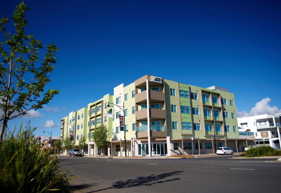a modern apartment building with a yellow facade and large windows under a clear blue sky at Quest Mawson Lakes
