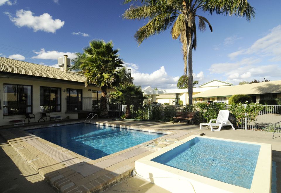 a large swimming pool with palm trees and lounge chairs is surrounded by a house at The Aston Motel Tamworth