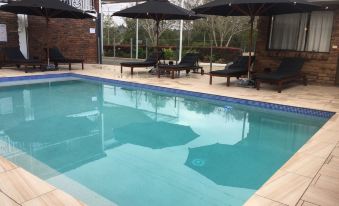 a large swimming pool with umbrellas and sun loungers around it , set in a sunny outdoor area at Logan City Motor Inn