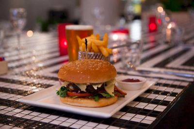 a dining table with a plate of food , including a burger , fries , and a drink at Ibis Melbourne Hotel and Apartments