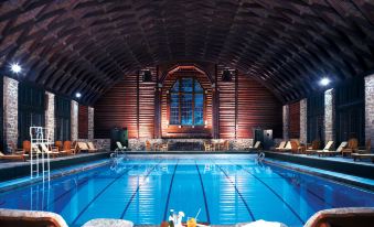 an indoor swimming pool with a wooden ceiling , surrounded by lounge chairs and a bar area at Fairmont le Château Montebello