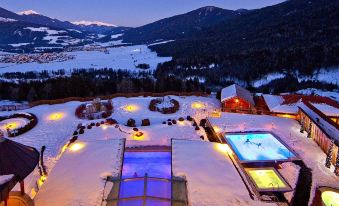 a snow - covered landscape with a large pool surrounded by buildings , and the sun is setting in the background at Alpin Panorama Hotel Hubertus