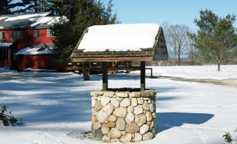 a snow - covered wooden structure with a stone base in front of a red building , and a small building in the background at Old Saco Inn