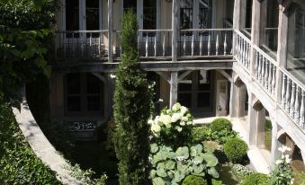 a courtyard with multiple buildings , including a large white building with balconies and stone walls , surrounded by lush greenery at Les Etangs de Corot