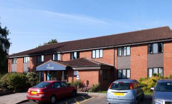 a brick building with multiple cars parked in front of it , creating a parking lot at Travelodge Ludlow Woofferton