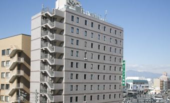 a modern , multi - story building with a green sign on the top and numerous balconies , situated in a bustling city street at Ace Inn Matsumoto