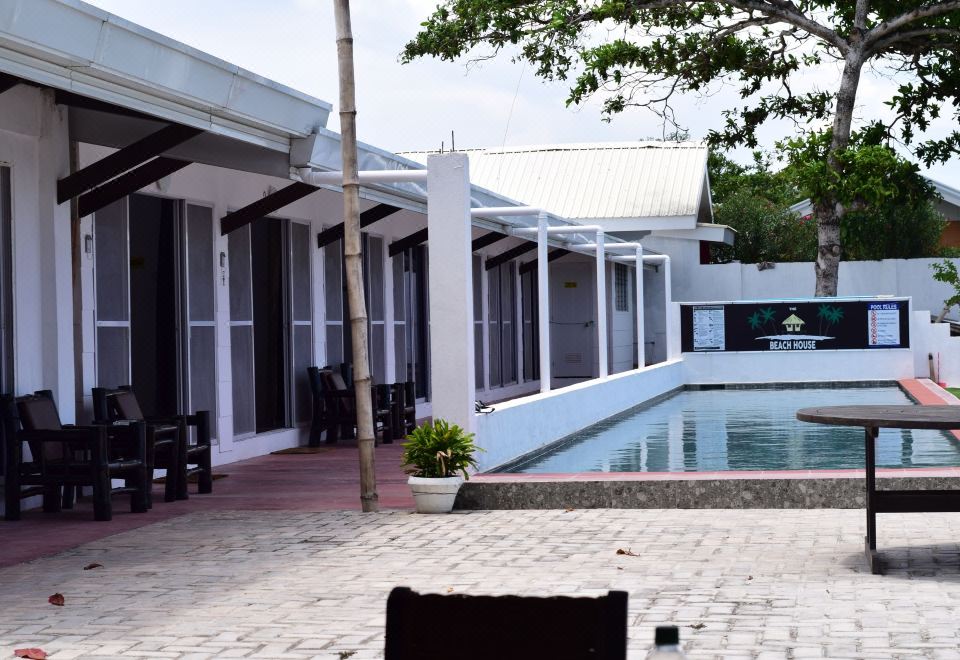 a small white building with a pool in front of it , surrounded by trees and grass at The Beachhouse