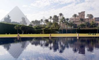 a large swimming pool with palm trees and a pyramid in the background , creating a serene atmosphere at Marriott Mena House, Cairo