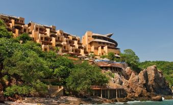 a cliffside resort with multiple buildings , trees , and a beach under a clear blue sky at Cala de Mar Resort & Spa Ixtapa
