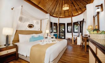 a luxurious bedroom with a canopy bed , wooden floors , and a dining table in the corner at Makunudu Island