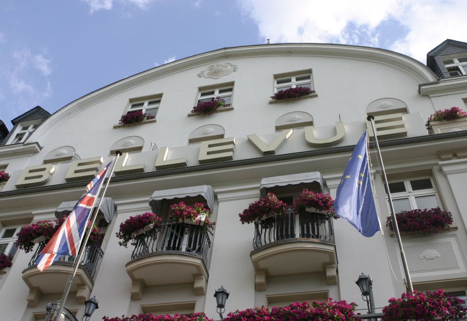 "a large white building with multiple balconies and flower arrangements , featuring the word "" clev "" written in gold letters" at Bellevue Rheinhotel