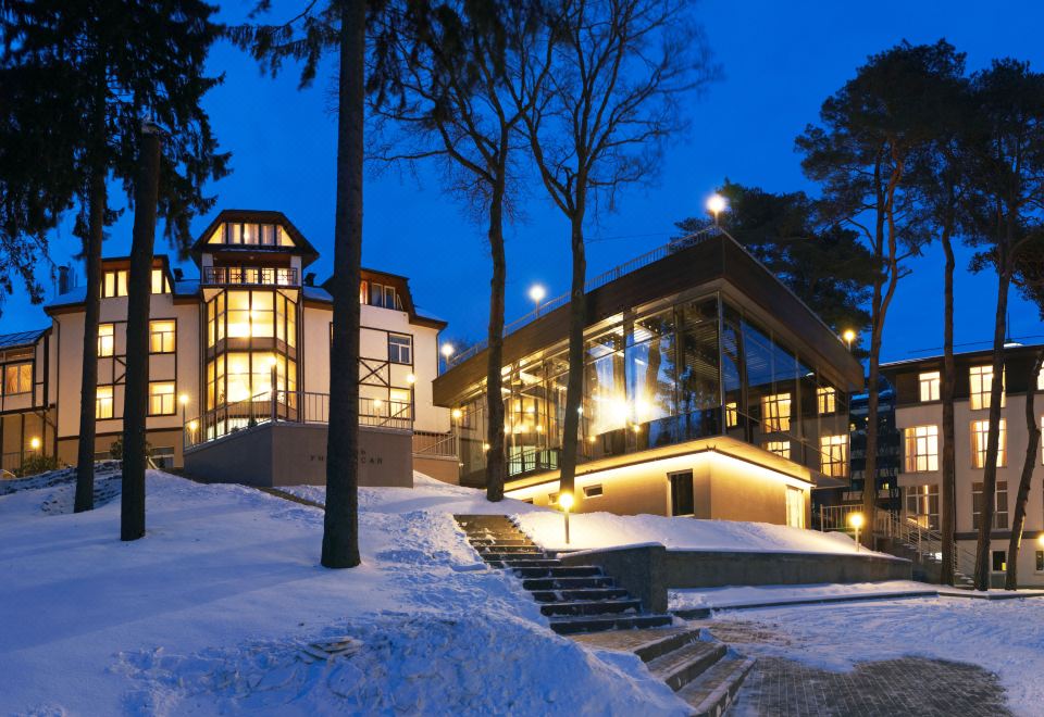 a snow - covered landscape with a large house surrounded by trees , lit up at night , and surrounded by snow at Universal Hotel