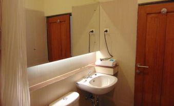 a bathroom with a white sink , toilet , and mirror , as well as a door leading to another room at Wisma BPI