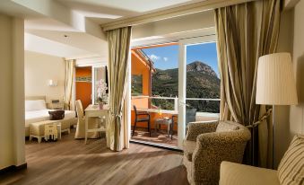 a spacious living room with a large window and sliding glass door , offering a view of the mountains at Boutique Hotel Torre di Cala Piccola